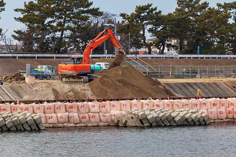 川岸で作業をするオレンジ色の油圧ショベル rifacimento argini modena